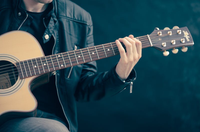 man playing acoustic guitar with his fingers pressing a chord on the frets